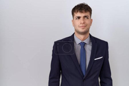 Foto de Joven hombre de negocios hispano vistiendo traje y corbata sonriendo mirando al costado y mirando hacia otro lado pensando. - Imagen libre de derechos
