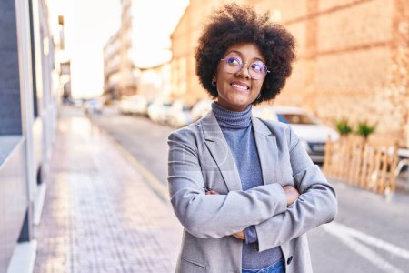 Téléchargez les photos : Femme afro-américaine exécutif souriant confiant debout avec les bras croisés geste à la rue - en image libre de droit