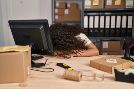 Foto de Joven mujer hispana hermosa comercio electrónico trabajador de negocios estresado con la cabeza en la mesa en la oficina - Imagen libre de derechos