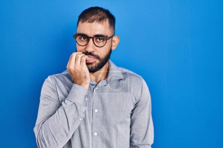 Photo for Middle east man with beard standing over blue background looking stressed and nervous with hands on mouth biting nails. anxiety problem. - Royalty Free Image