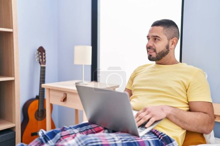 Photo for Young latin man using laptop sitting on bed at bedroom - Royalty Free Image