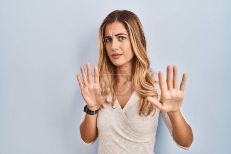 Photo for Young blonde woman standing over isolated background moving away hands palms showing refusal and denial with afraid and disgusting expression. stop and forbidden. - Royalty Free Image