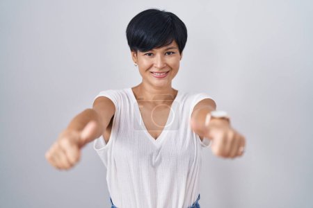 Téléchargez les photos : Jeune femme asiatique avec les cheveux courts debout sur fond isolé approuvant faire un geste positif avec la main, pouces levés souriant et heureux pour le succès. geste gagnant. - en image libre de droit