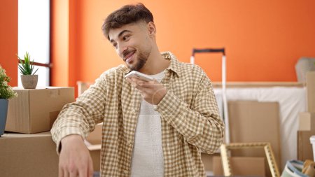Foto de Hombre árabe joven sonriendo confiado enviando mensaje de voz por teléfono inteligente en un nuevo hogar - Imagen libre de derechos