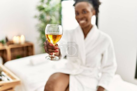 Téléchargez les photos : Femme afro-américaine portant un peignoir buvant du champagne au salon de beauté - en image libre de droit