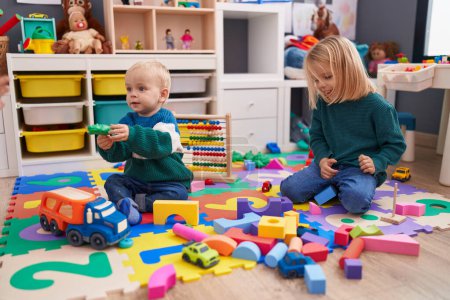 Téléchargez les photos : Adorable garçon et fille jouant avec des blocs de construction assis sur le sol à la maternelle - en image libre de droit