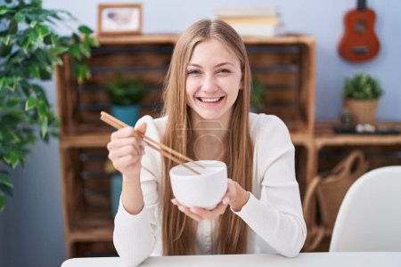 Photo for Young caucasian woman eating asian food using chopsticks winking looking at the camera with sexy expression, cheerful and happy face. - Royalty Free Image