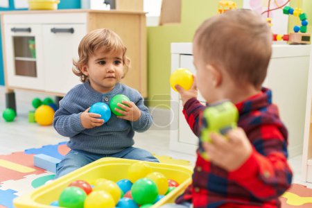 Téléchargez les photos : Adorables garçons jouant avec des balles et des jouets de voiture assis sur le sol à la maternelle - en image libre de droit