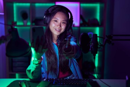 Photo for Young asian woman playing video games with smartphone approving doing positive gesture with hand, thumbs up smiling and happy for success. winner gesture. - Royalty Free Image