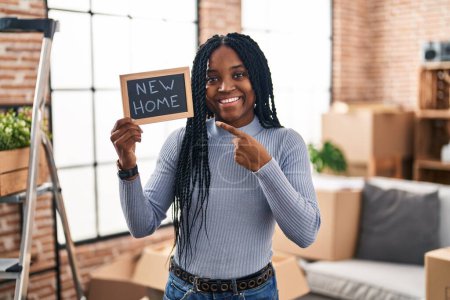 Téléchargez les photos : Afro-américaine femme tenant tableau noir avec nouveau texte à la maison souriant heureux pointant avec la main et le doigt - en image libre de droit