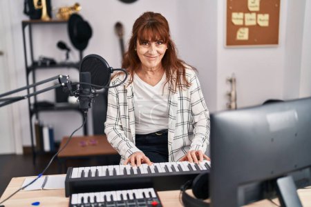 Téléchargez les photos : Femme musicienne d'âge moyen jouant du clavier de piano au studio de musique - en image libre de droit