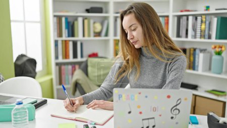 Téléchargez les photos : Jeune étudiante caucasienne utilisant l'écriture d'ordinateur portable sur ordinateur portable à l'université de la bibliothèque - en image libre de droit