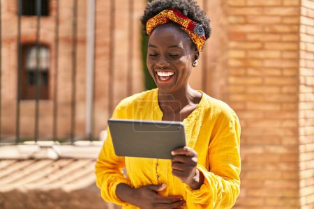 Téléchargez les photos : Jeune femme afro-américaine souriante confiante regarder la vidéo sur touchpad à la rue - en image libre de droit