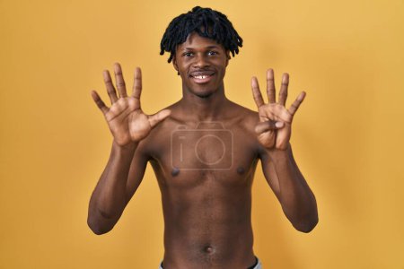 Téléchargez les photos : Jeune homme africain avec dreadlocks debout torse nu montrant et pointant vers le haut avec les doigts numéro neuf tout en souriant confiant et heureux. - en image libre de droit