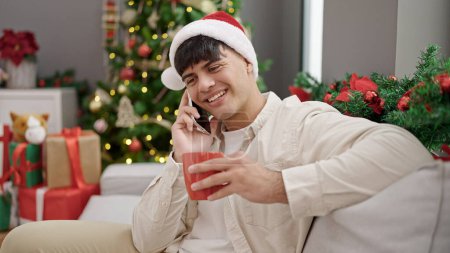 Photo for Young hispanic man talking on smartphone drinking coffee celebrating christmas at home - Royalty Free Image