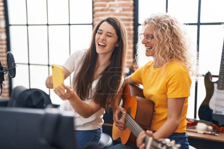 Téléchargez les photos : Deux femmes musiciens jouant de la guitare classique regardant l'écran du smartphone au studio de musique - en image libre de droit