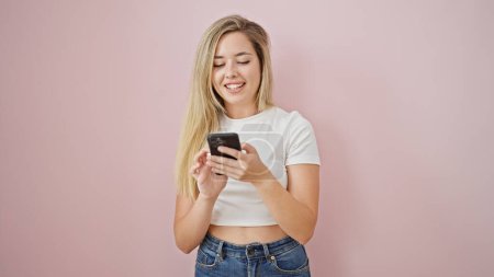Téléchargez les photos : Jeune femme blonde utilisant smartphone souriant sur fond rose isolé - en image libre de droit