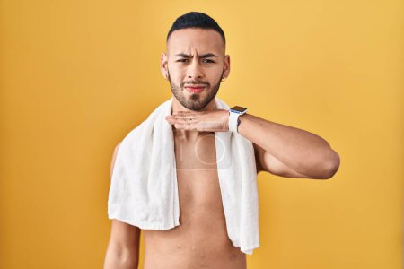 Téléchargez les photos : Jeune homme hispanique debout torse nu avec une serviette tranchant la gorge avec la main comme un couteau, menace d'agression avec une violence furieuse - en image libre de droit