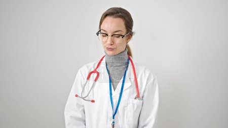 Foto de Mujer joven caucásica médico de pie con expresión seria mirando hacia abajo sobre el fondo blanco aislado - Imagen libre de derechos