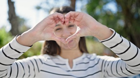Téléchargez les photos : Jeune belle femme hispanique souriant confiant faire geste de coeur avec les mains au parc - en image libre de droit
