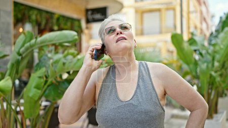 Foto de Mujer de pelo gris de mediana edad hablando en el teléfono inteligente con expresión seria en el parque - Imagen libre de derechos