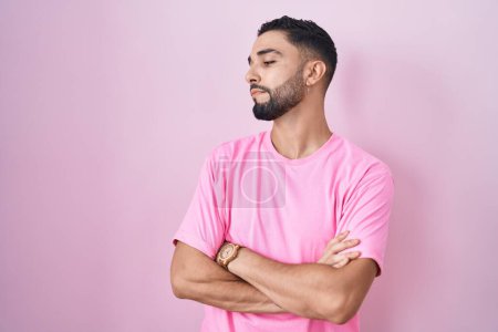 Téléchargez les photos : Jeune homme hispanique debout sur fond rose regardant du côté avec les bras croisés convaincu et confiant - en image libre de droit