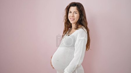 Téléchargez les photos : Jeune femme enceinte souriant confiant toucher le ventre sur fond rose isolé - en image libre de droit