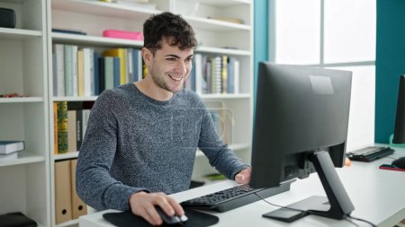 Téléchargez les photos : Jeune homme hispanique étudiant utilisant l'ordinateur souriant à l'université de la bibliothèque - en image libre de droit