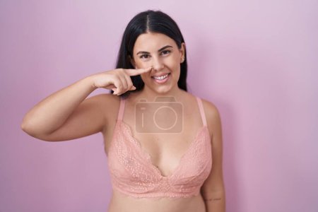 Téléchargez les photos : Jeune femme hispanique portant un soutien-gorge rose pointant avec le doigt de la main sur le visage et le nez, souriant gai. concept de beauté - en image libre de droit