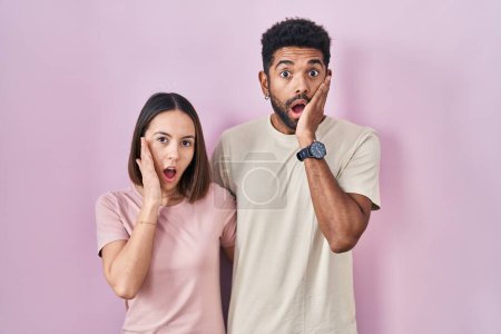 Photo for Young hispanic couple together over pink background afraid and shocked, surprise and amazed expression with hands on face - Royalty Free Image