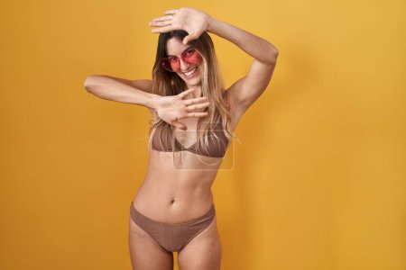 Foto de Young hispanic woman wearing bikini over yellow background smiling cheerful playing peek a boo with hands showing face. surprised and exited - Imagen libre de derechos