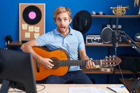 Foto de Hombre caucásico tocando la guitarra clásica en el estudio de música en la cara de choque, mirando escéptico y sarcástico, sorprendido con la boca abierta - Imagen libre de derechos