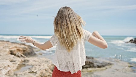 Foto de Joven mujer rubia turista de pie al revés bailando en la playa - Imagen libre de derechos