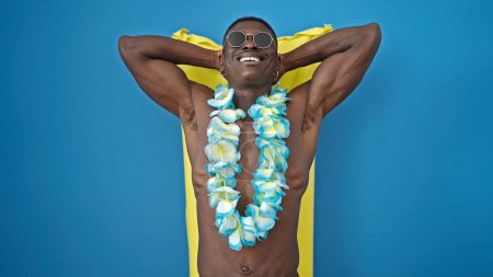 Téléchargez les photos : Africain américain touriste debout torse nu portant hawaiian lei sur matelas flottant sur fond bleu isolé - en image libre de droit