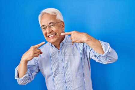 Photo for Hispanic senior man wearing glasses smiling cheerful showing and pointing with fingers teeth and mouth. dental health concept. - Royalty Free Image