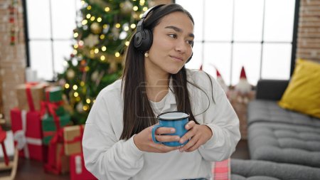 Foto de Joven mujer hispana hermosa escuchando música bebiendo café celebrando la Navidad en casa - Imagen libre de derechos