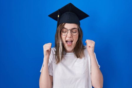 Photo for Blonde caucasian woman wearing graduation cap excited for success with arms raised and eyes closed celebrating victory smiling. winner concept. - Royalty Free Image