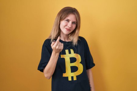 Photo for Blonde caucasian woman wearing bitcoin t shirt beckoning come here gesture with hand inviting welcoming happy and smiling - Royalty Free Image