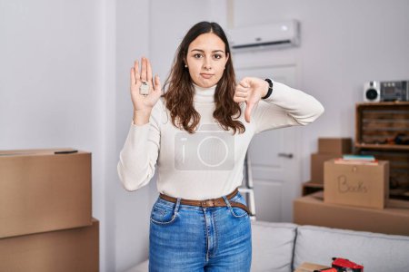 Photo for Young hispanic woman holding keys of new home with angry face, negative sign showing dislike with thumbs down, rejection concept - Royalty Free Image