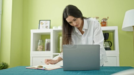Foto de Mujer hispana hermosa joven usando la escritura del ordenador portátil en el portátil en el comedor - Imagen libre de derechos