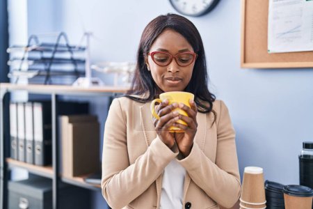 Téléchargez les photos : Jeune femme d'affaires afro-américaine buvant du café au bureau - en image libre de droit