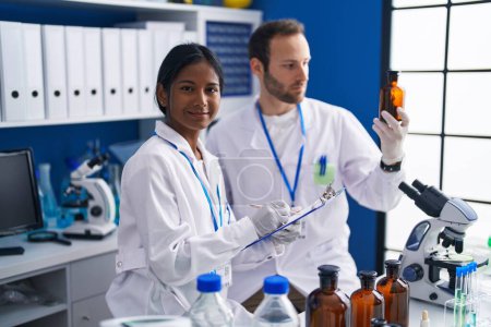 Photo for Man and woman scientists holding bottle writing report at laboratory - Royalty Free Image