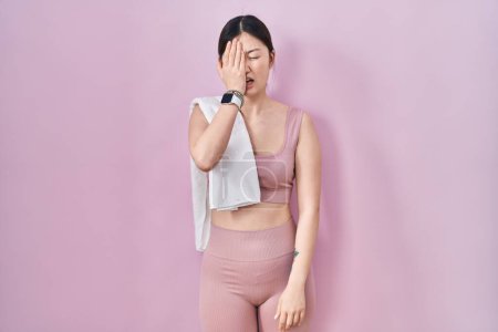 Foto de Mujer joven china con ropa deportiva y toalla bostezando cansada cubriendo media cara, ojo y boca con la mano. cara duele en el dolor. - Imagen libre de derechos
