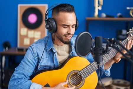 Photo for Young hispanic man artist singing song playing classical guitar at music studio - Royalty Free Image