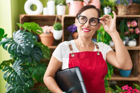 Téléchargez les photos : Jeune belle hispanique femme fleuriste souriant confiant tenant liant à la boutique de fleurs - en image libre de droit