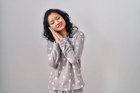 Téléchargez les photos : Jeune femme asiatique portant un pyjama dormir fatigué rêvant et posant avec les mains ensemble tout en souriant avec les yeux fermés. - en image libre de droit