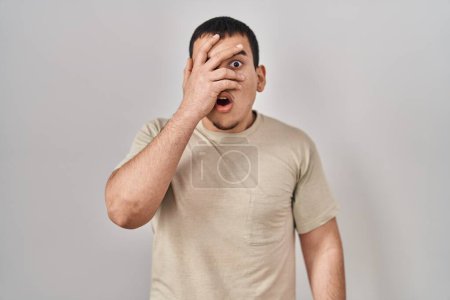 Téléchargez les photos : Jeune homme arabe portant t-shirt décontracté jetant un coup d'oeil dans le visage de couverture de choc et les yeux avec la main, regardant à travers les doigts avec une expression embarrassée. - en image libre de droit