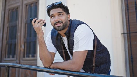 Téléchargez les photos : Homme afro-américain écoutant un message audio par le smartphone avec une expression sérieuse dans la rue - en image libre de droit