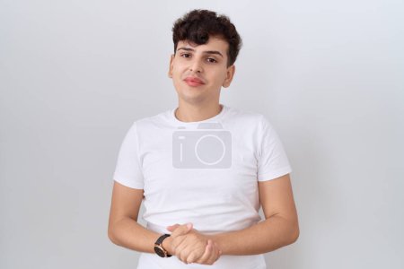 Téléchargez les photos : Jeune homme non binaire portant t-shirt blanc décontracté avec les mains ensemble et les doigts croisés souriant détendu et joyeux. succès et optimisme - en image libre de droit