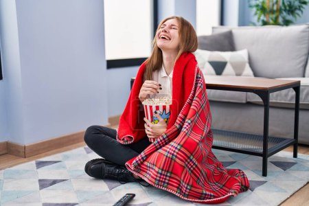 Téléchargez les photos : Jeune femme blonde regarder un film assis sur le sol à la maison - en image libre de droit